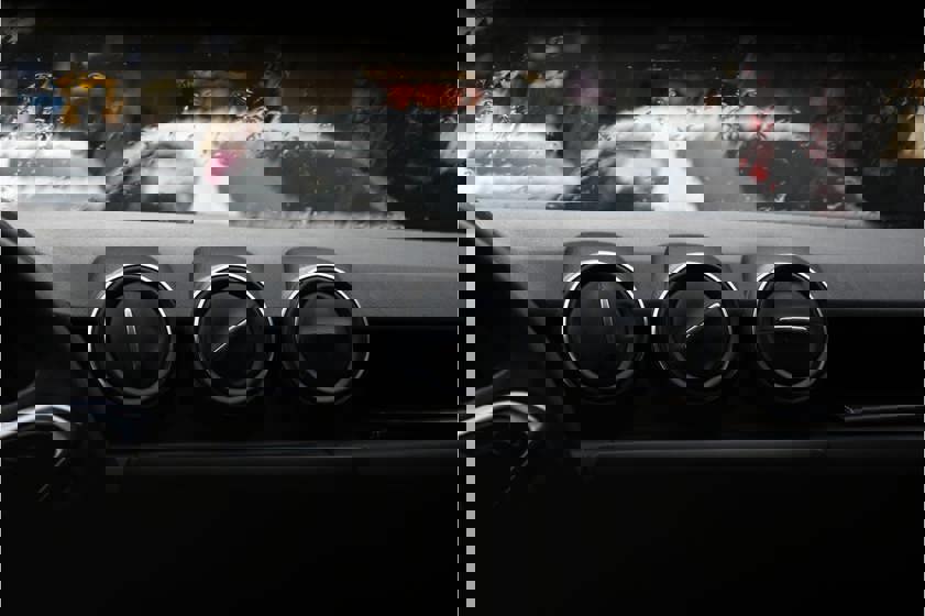Three air vents sitting on top of a car dashboard with a rainy windscreen in the background