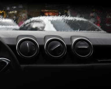 Three air vents sitting on top of a car dashboard with a rainy windscreen in the background
