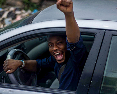 young driver in the car looking happy with his arm raised out of the window in joy