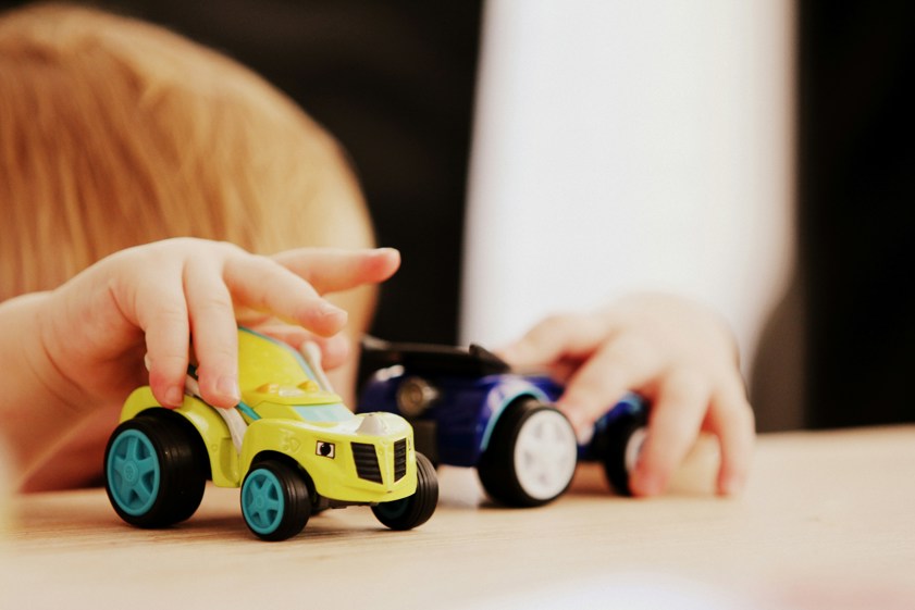 child playing with two assorted colour car plastic toys on brown wooden table
