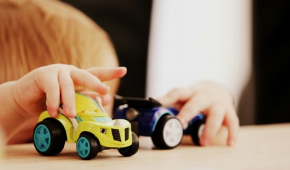 child playing with two assorted colour car plastic toys on brown wooden table
