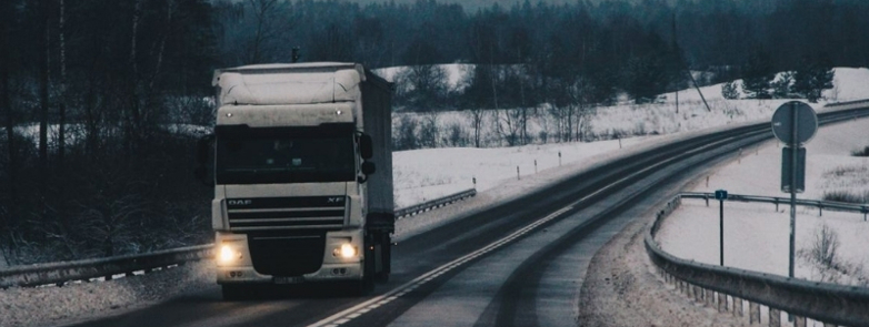 A cargo truck travels on a snowy countryside road during winter, showcasing rural transportation.