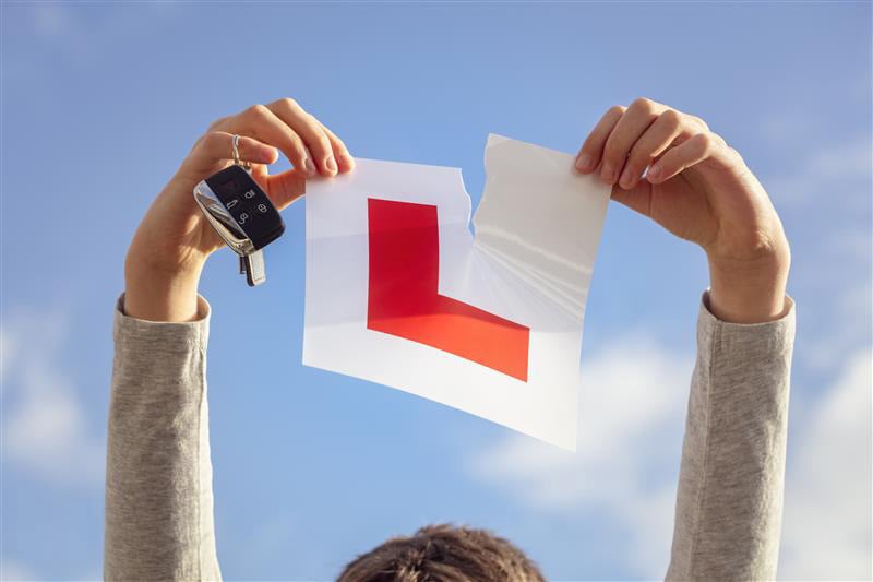 Person holding ripped UK learner driver L-plate and car keys against blue sky, symbolising passing driving test and gaining full licence