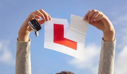 Person holding ripped UK learner driver L-plate and car keys against blue sky, symbolising passing driving test and gaining full licence