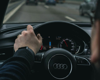 Person driving an Audi car on the motorway with one hand on the wheel