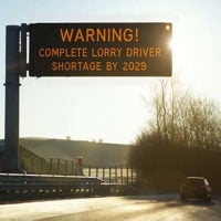 a motorway digital sign at sunrise warning drivers with the message: "WARNING! COMPLETE LORRY DRIVER SHORTAGE BY 2029.