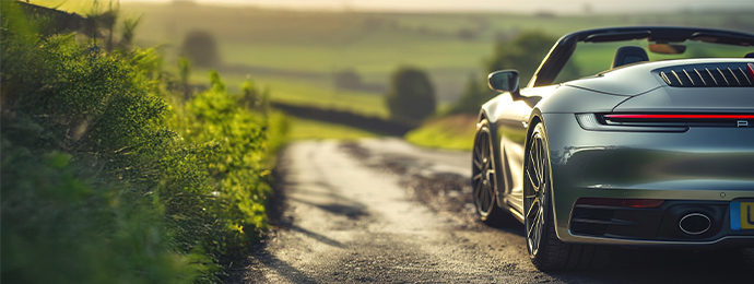 Rear close-up of a Porsche 911 convertible on a winding UK country road at sunset