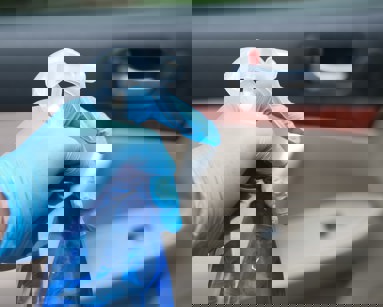 hand in gloves holding spray bottle cleaning car door