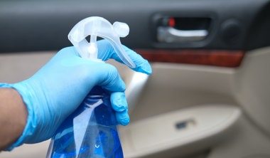 hand in gloves holding spray bottle cleaning car door