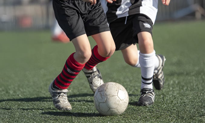 Photorealistic close-up sports action photo of two 8 year old footballers’ lower legs battling for a worn off-white football,