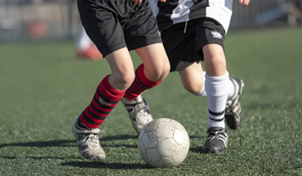 Photorealistic close-up sports action photo of two 8 year old footballers’ lower legs battling for a worn off-white football,
