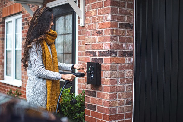 Woman plugging electric car into household charging port 