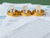 Staged image of gold coins with tax letter tiles on documents.