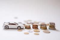 White toy sports car beside stacks of coins on a white background, emphasizing savings and finance