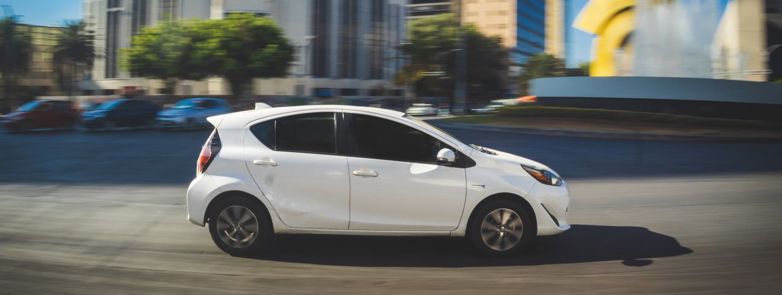 A white car in motion against a backdrop of urban architecture and sculptures.