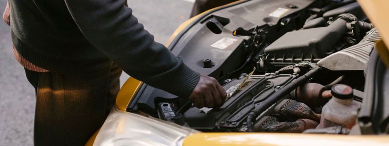 Two mechanics examining and fixing the engine of a yellow taxi cab on the road.