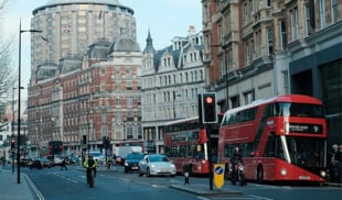 Street scene in London featuring iconic red buses, historic buildings, and urban life.
