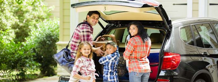 Smiling family packing a car boot on a sunny day