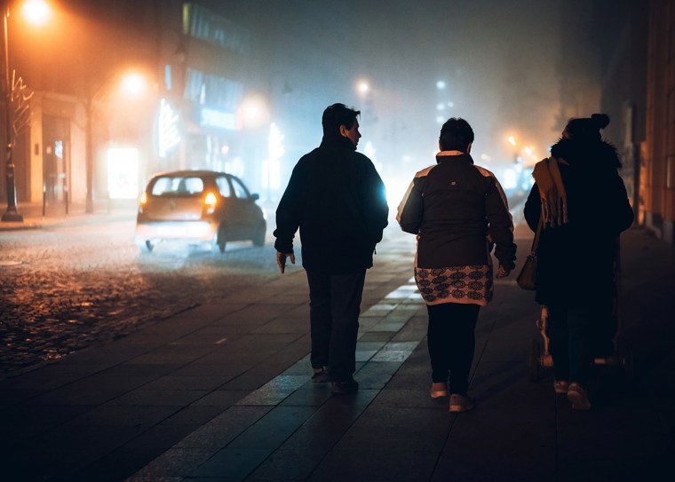 Three people walking alongside road at night