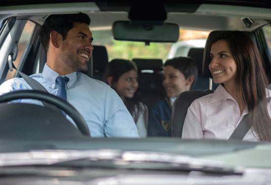 Happy parents taking their kids to school in car while looking at each other smiling very lovingly