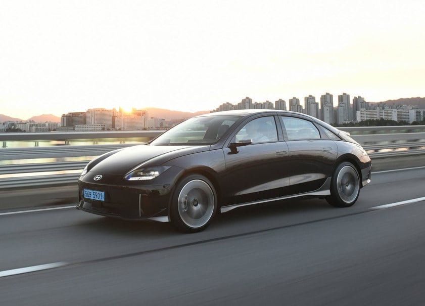 Hyundai Ioniq 6 in black driving over a bridge with high rise buildings in the background