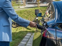 Person connecting an electric car to a charging station outdoors, showcasing green energy transition