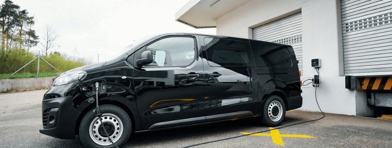 A black van plugged into charge while being parked in front of a garage.