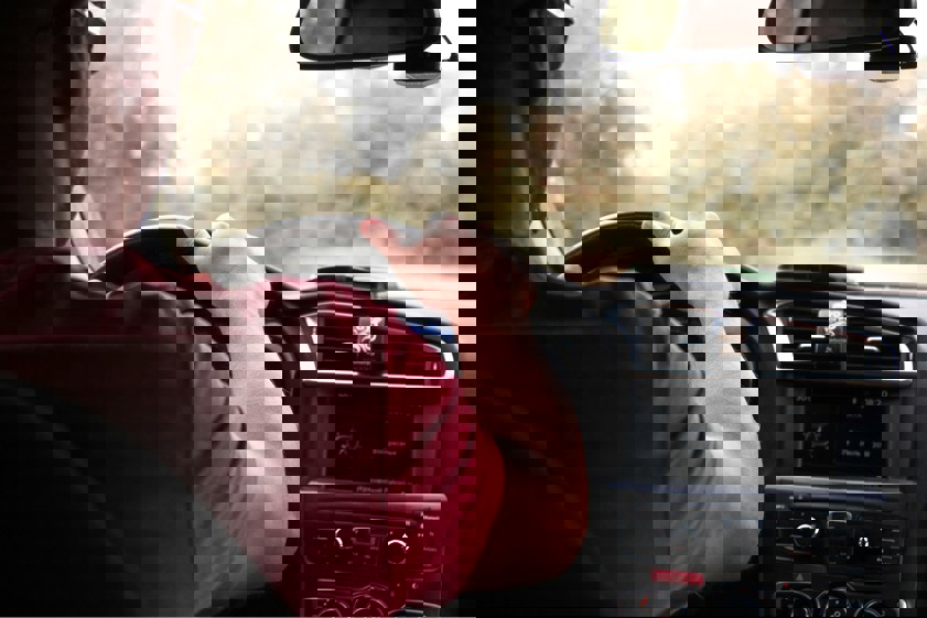 Man in red top driving car with hand on the steering wheel