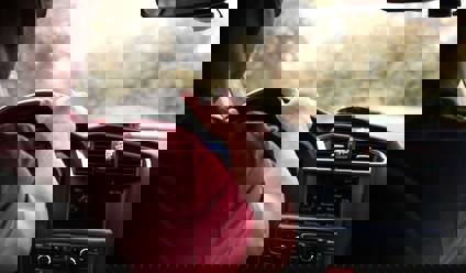 Man in red top driving car with hand on the steering wheel