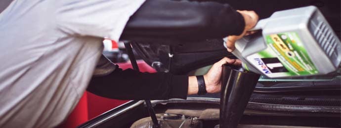 Man refilling motor oil on car engine bay