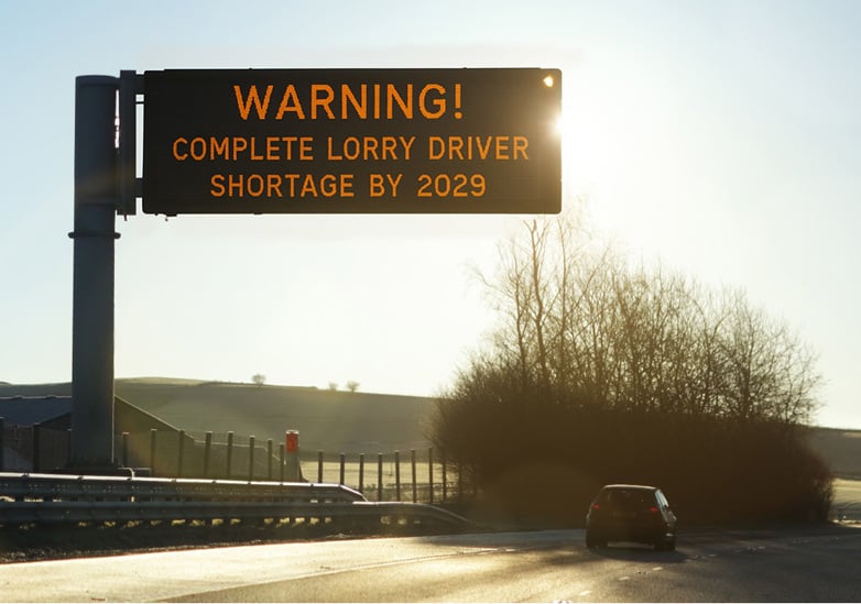 a motorway digital sign at sunrise warning drivers with the message: "WARNING! COMPLETE LORRY DRIVER SHORTAGE BY 2029.