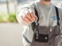 Hand holding a car key outdoors, blurred background, shallow focus.