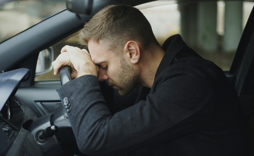 man resting head on steering wheel in car