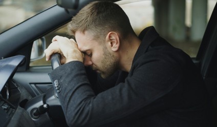 man resting head on steering wheel in car
