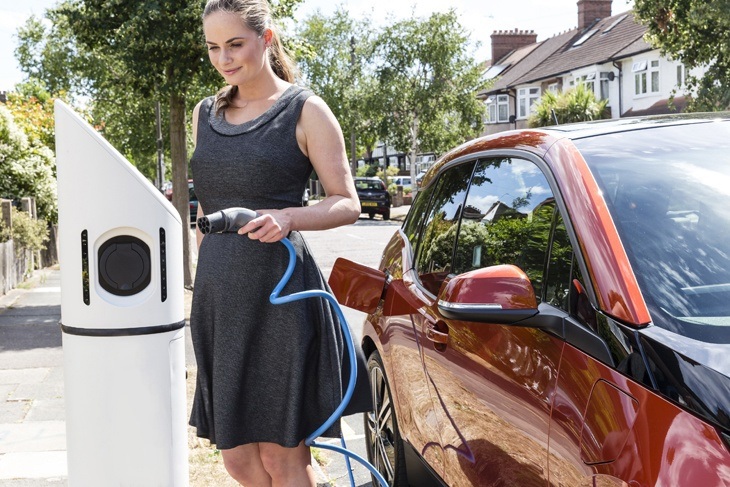 Woman on sunny street charging an electric car at roadside