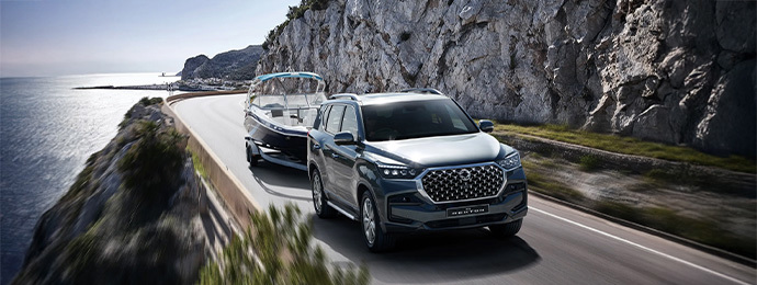 KG Mobility Rexton SUV towing a speedboat along a coastal mountain road