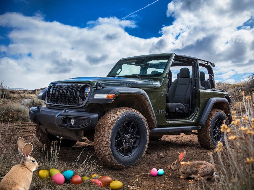 Green Jeep Wrangler with doors off parked on a muddy trail, surrounded by Easter eggs and rabbits