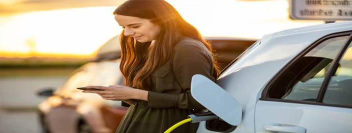 Woman checking her phone while charging an electric car