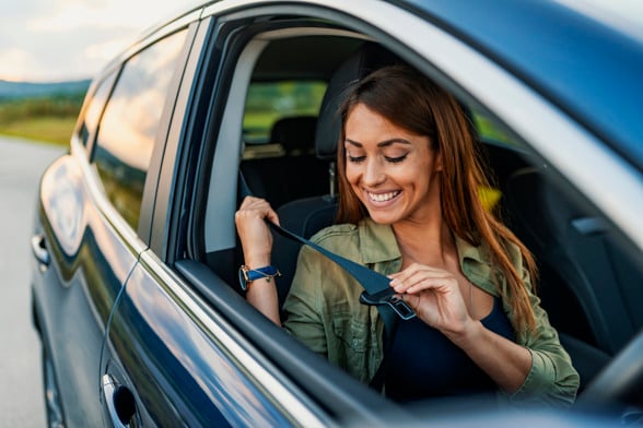 business woman sitting in a car putting on her seat belt