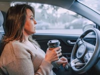 A woman in a car holding a disposable coffee cup, showing focus