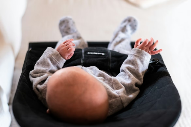 baby wearing grey onesie on black bouncer