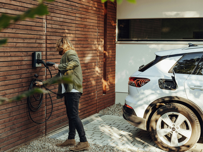 Man charging white electric SUV at home EV wall charger