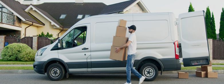 Man unloading cardboard boxes from a delivery van in a suburban neighbourhood street