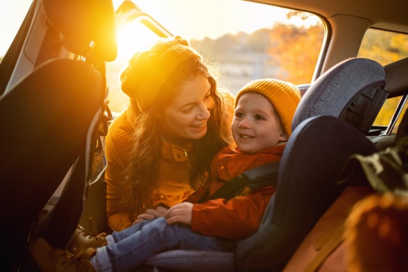 mother fastening her son safely in a car seat.