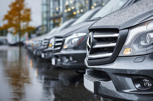 A photorealistic image of a row of mercedes-benz new vans parked at a UK-style dealership, blurred with large glass windows.