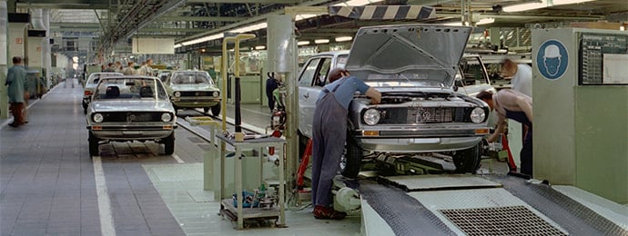 Historic image of a Volkswagen Polo production line in a factory during the 1970s, showing assembly workers building early Polo models.