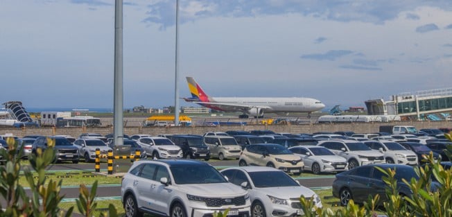 aeroplane taxiing on runway with cars in foreground