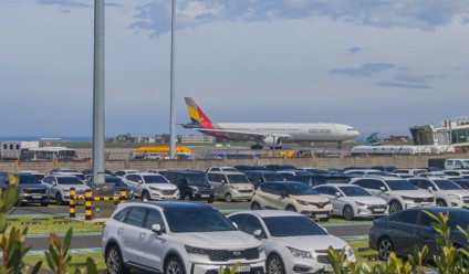 aeroplane taxiing on runway with cars in foreground