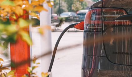 Close-up of an electric car charging at a station with blurred cars in the background.