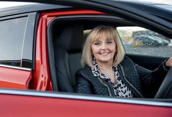 Mature caucasian woman smiling at the camera as she gets out of her car.
